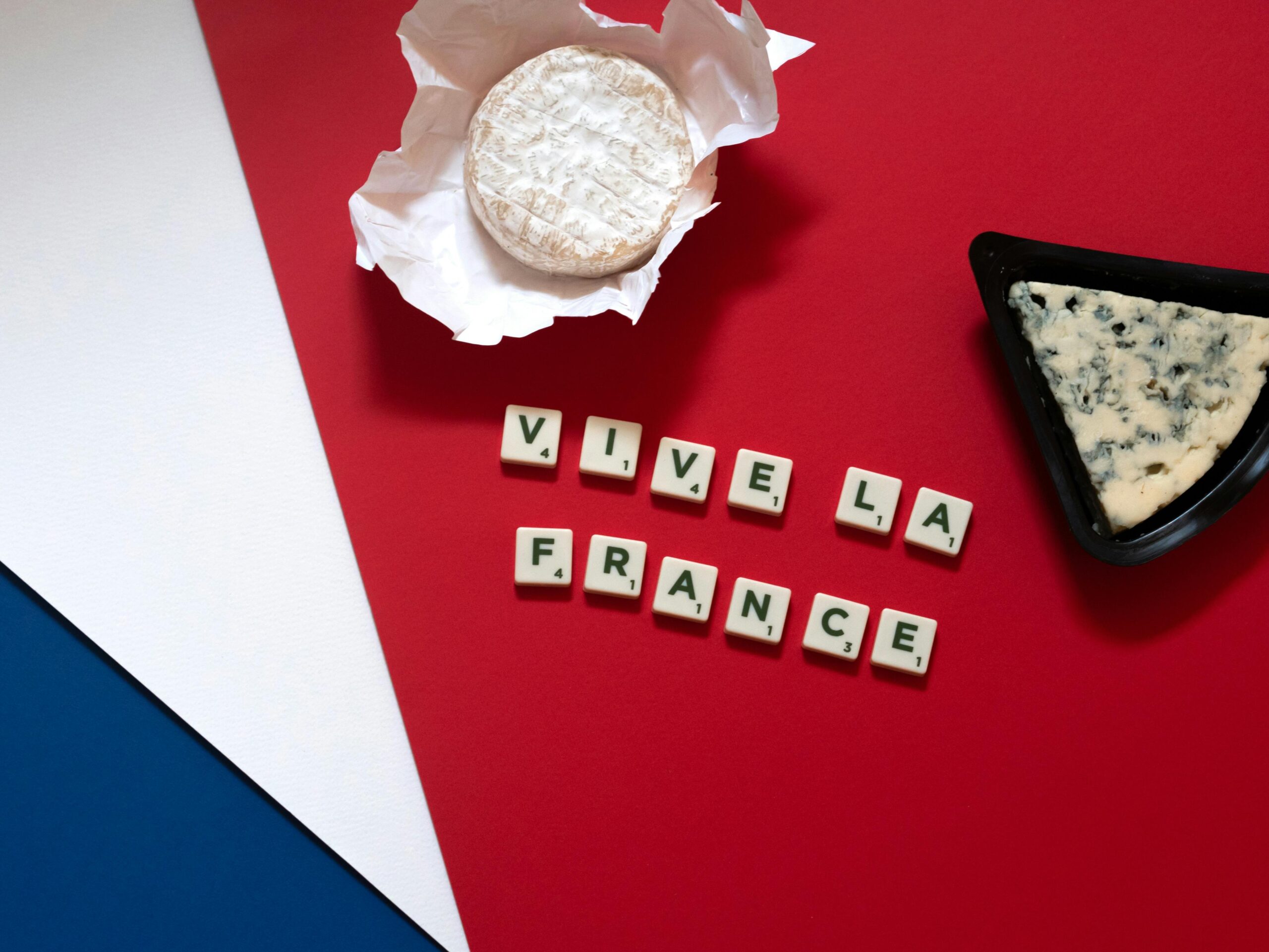 Colorful composition of French cheese and scrabble tiles forming 'Vive La France' on a tricolor background.